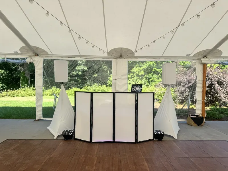 A white wedding DJ booth with speakers under a tent